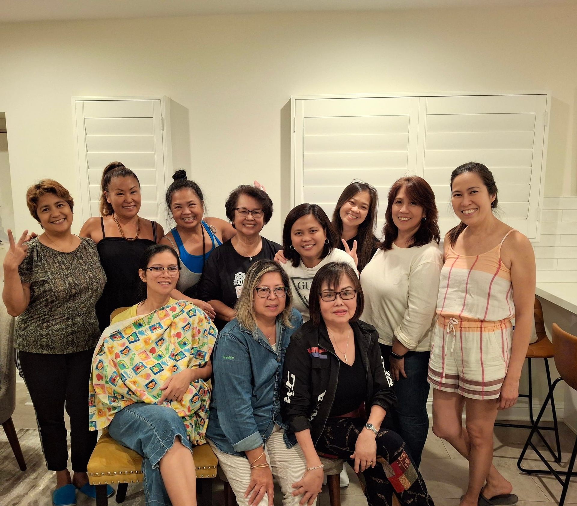 Group of women posing together in a living room, with some standing and others seated on stools.