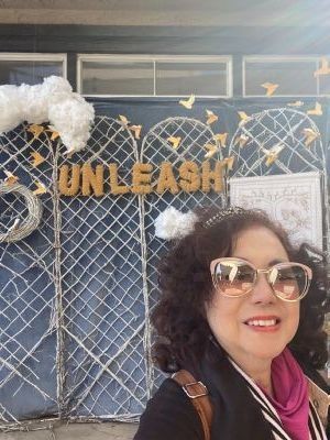 Woman smiling in front of decorative backdrop with the word 'UNLEASH' and paper birds.