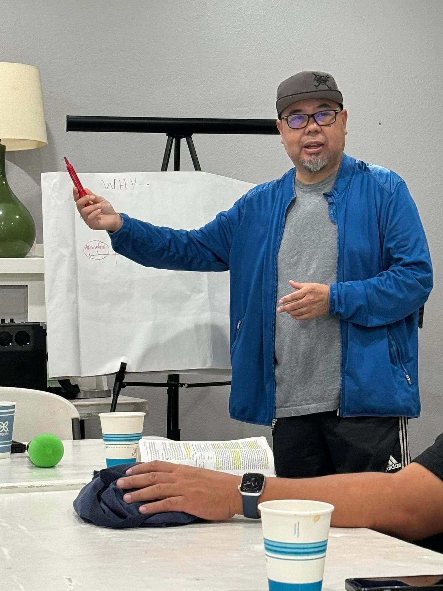 Person in a blue jacket giving a presentation, pointing at a paper on an easel.