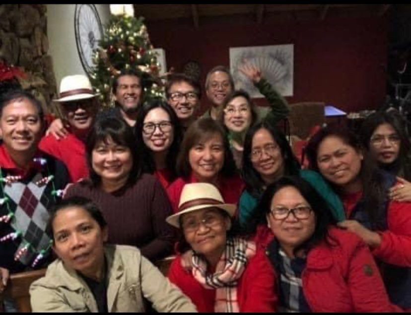 Group of people smiling in front of a decorated Christmas tree indoors.