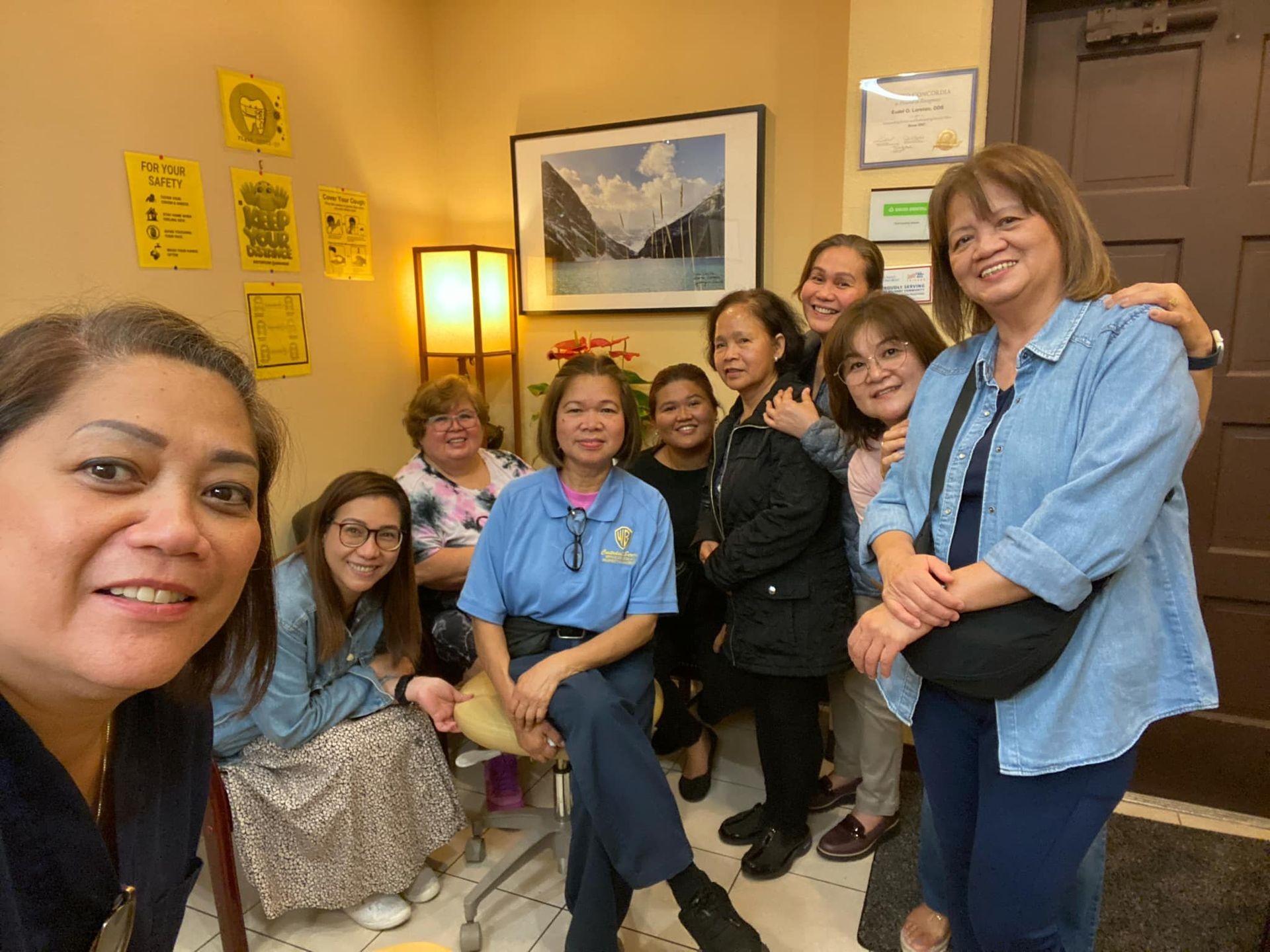Group of smiling people posing in a cozy room with yellow wall posters and a lamp.