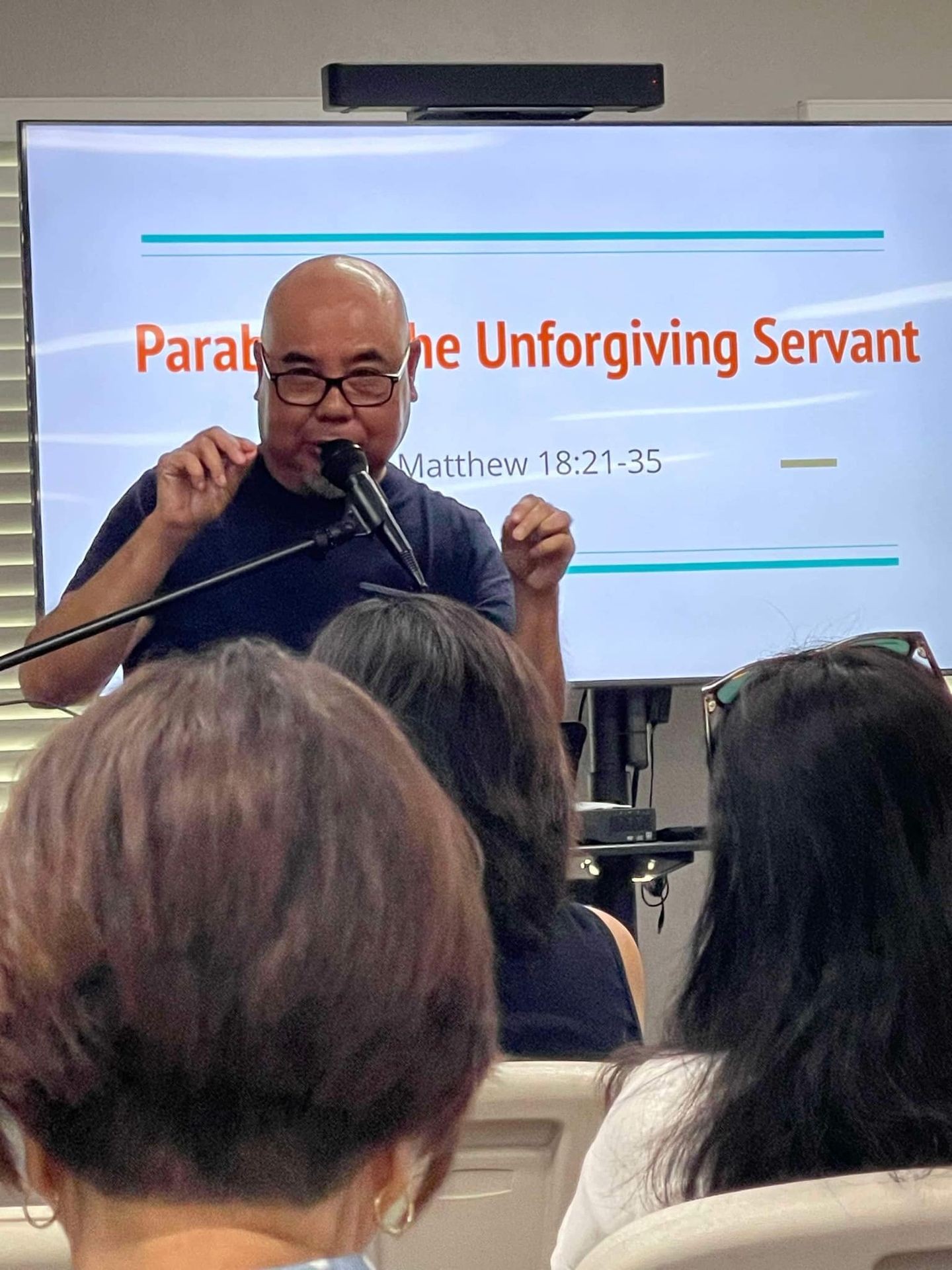 Speaker presenting about 'The Unforgiving Servant' with audience in a classroom setting.